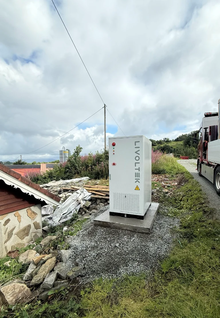 Batteriskap fra Livoltek på et betongfundament ved gårdsbygningen, med en kraftlinje i bakgrunnen