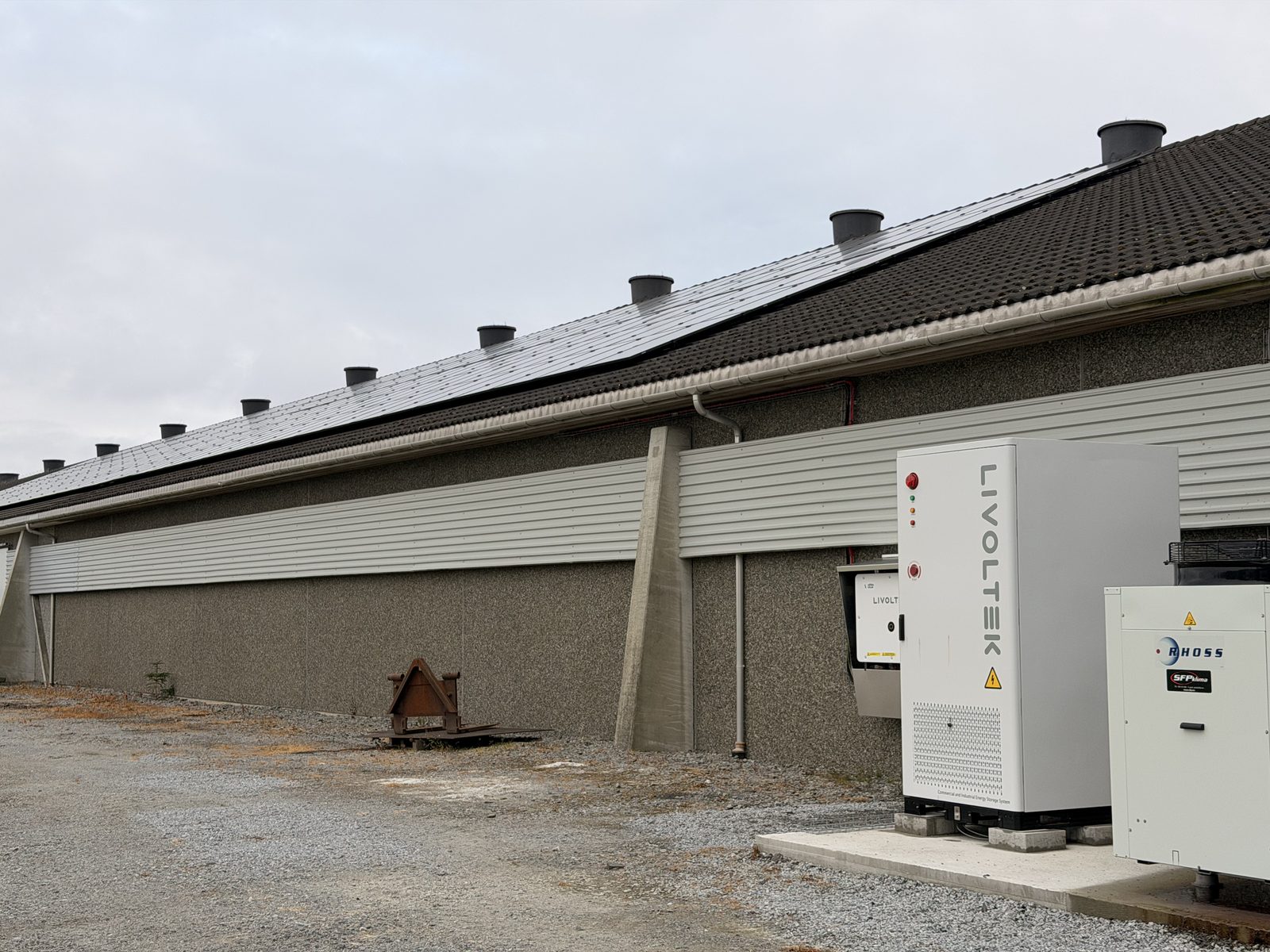 Den lange fasaden på kyllinghuset med solceller langs hele takflaten, og batteriskapet og varmepumpen stående på et fundament ved veggen