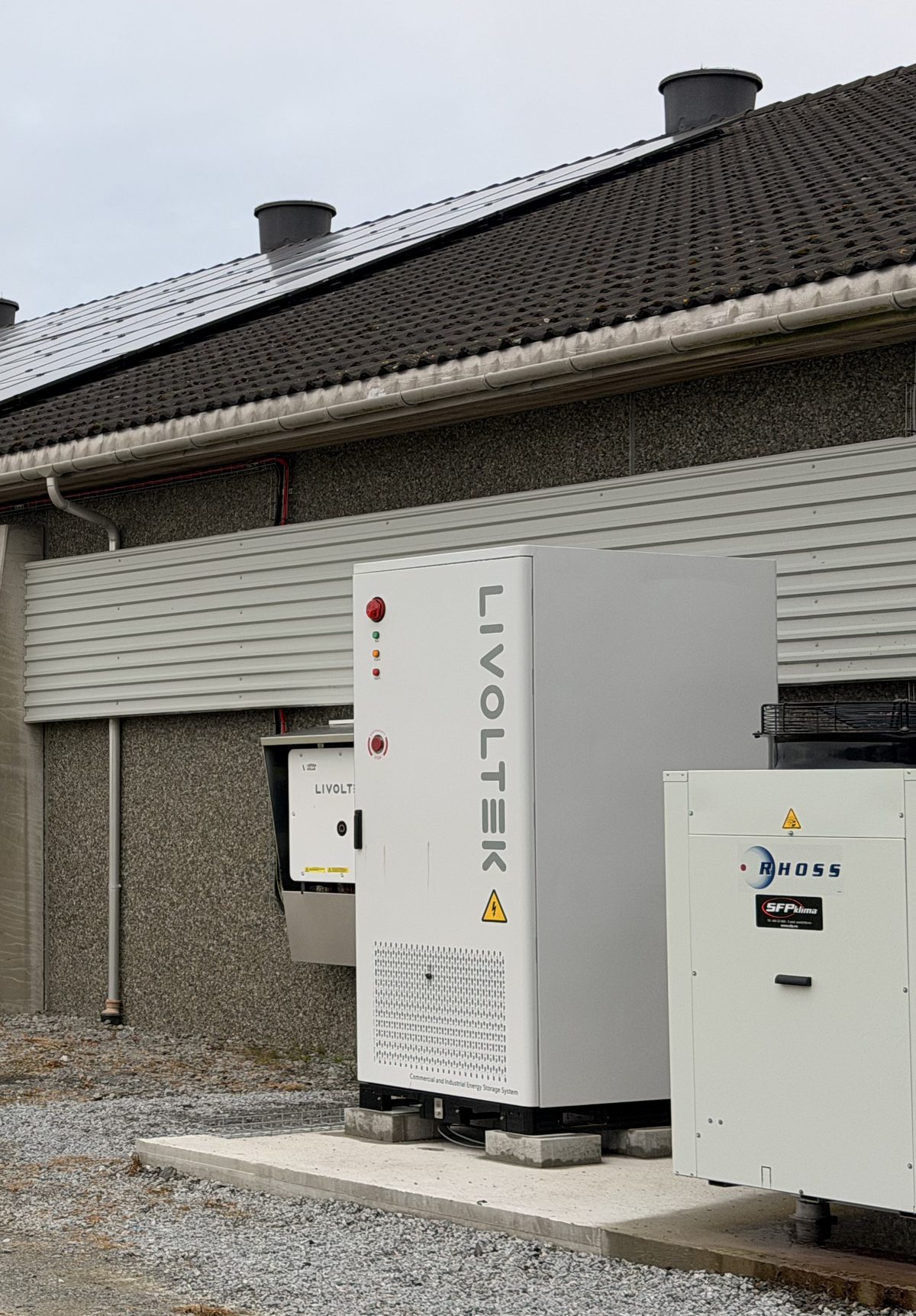 Det hvite batteriskapet og varmepumpen montert på et fundament langs veggen på kyllinghuset