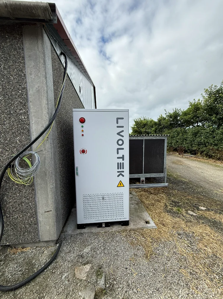 Hvitt batteriskap fra Livoltek på et betongfundament inntil veggen på en driftsbygning på melkegården