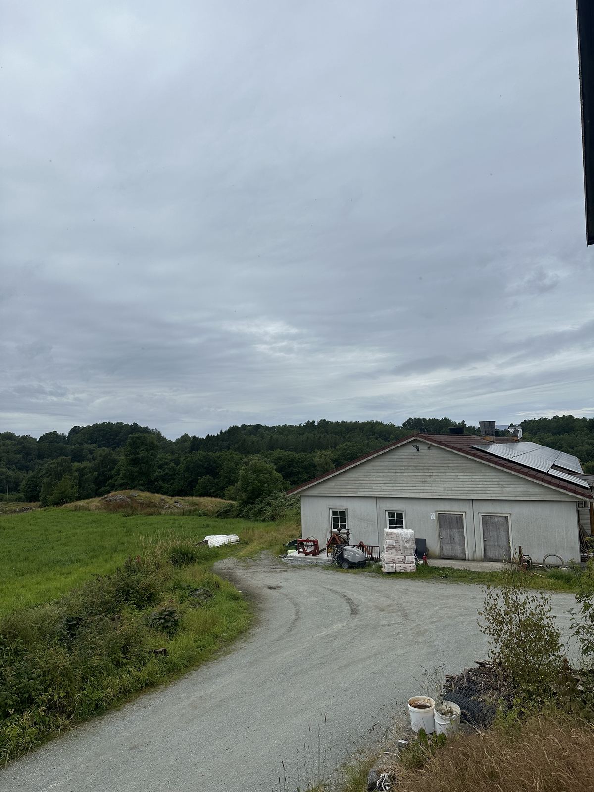 Gårdsbygningen med solceller på taket, med skog og beite rundt