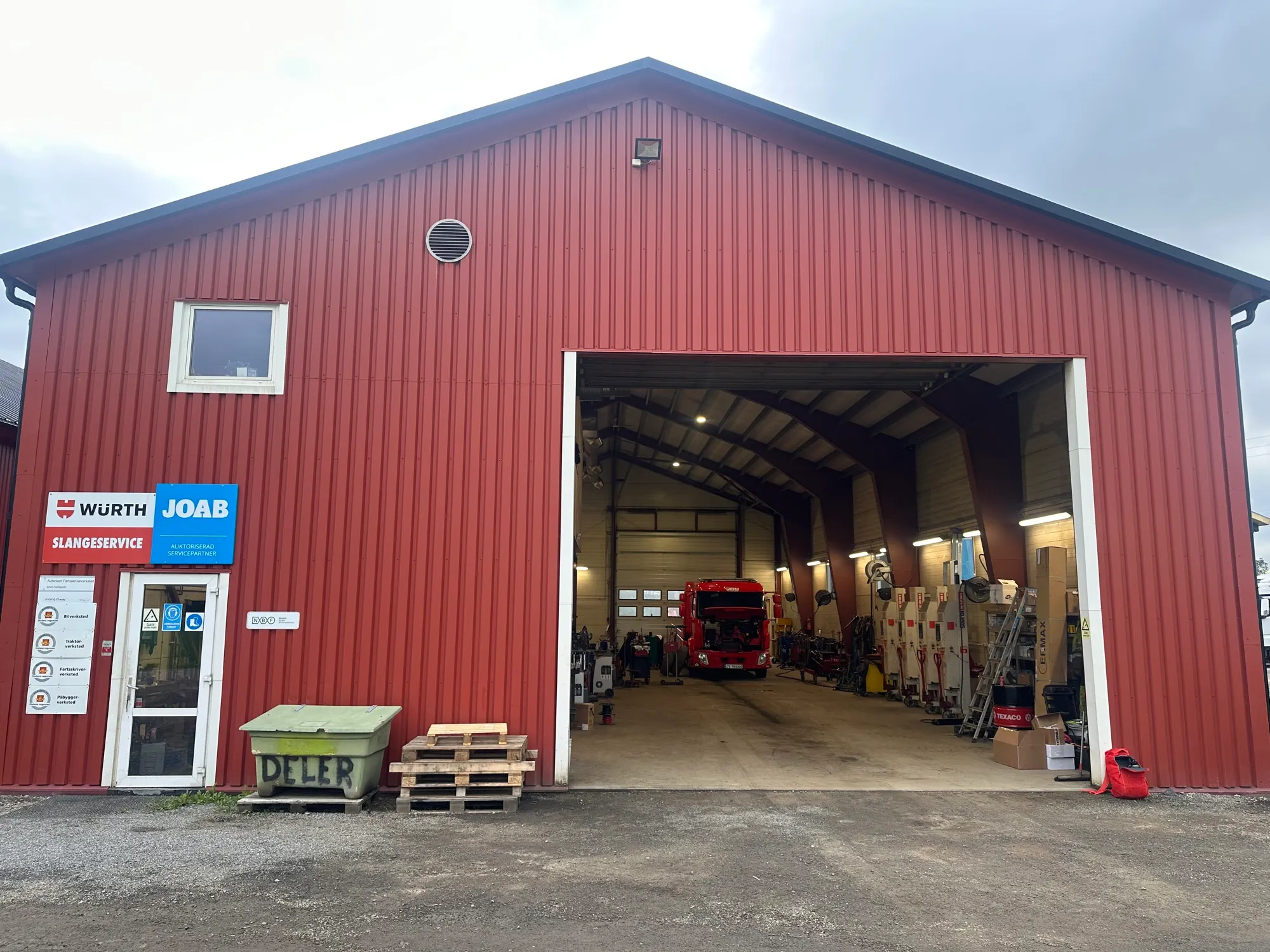 Den røde verkstedhallen på Trettemo med stor port åpen og en lastebil inne til service
